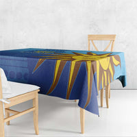 Blue tablecloth draped over dining table with large yellow sun face artwork