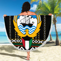 Round black beach blanket held open, featuring Kuwait hawk emblem with fringed white border