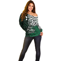 Women's off-shoulder green sweater with white tribal design, long sleeves
