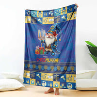 Blue blanket featuring a gnome holding gifts, menorah patterns, and “Happy Chrismukkah”