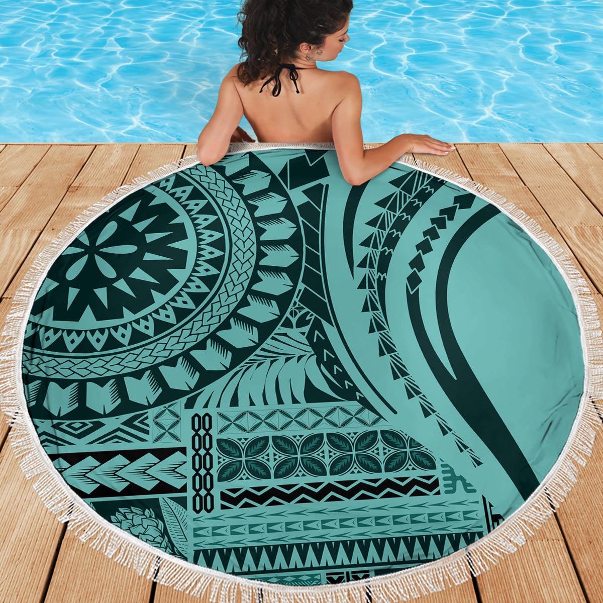 Round turquoise patterned beach blanket with white fringe on wooden deck