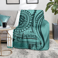 Turquoise patterned blanket draped on chair, black mandala, stripes, and leaf motifs
