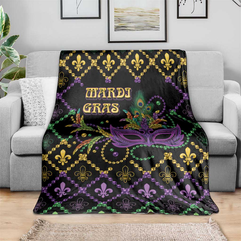 Black geometric Mardi Gras blanket spread on couch, purple mask center, fleur-de-lis and beads.