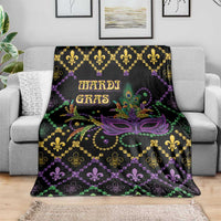 Black geometric Mardi Gras blanket spread on couch, purple mask center, fleur-de-lis and beads.