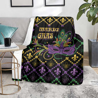 Black geometric Mardi Gras blanket on rug, purple mask, green bead strands, fleur-de-lis.