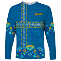 Blue long-sleeve shirt with Scandinavian cross pattern, birds and flowers; yellow 'Your text'.