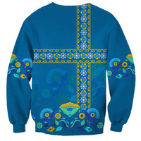 Blue crewneck sweatshirt with large yellow cross folk print, birds and flowers on back.