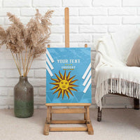 Blue canvas wall art on easel with sun emblem and “YOUR TEXT” Uruguay lettering.