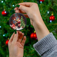 Black round ceramic Christmas ornament with Santa hugging a moose, held in a hand by a string.