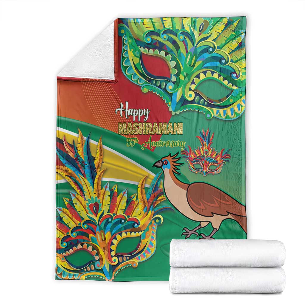 Green Mashramani anniversary blanket with bird and mask artwork, stacked with white towels