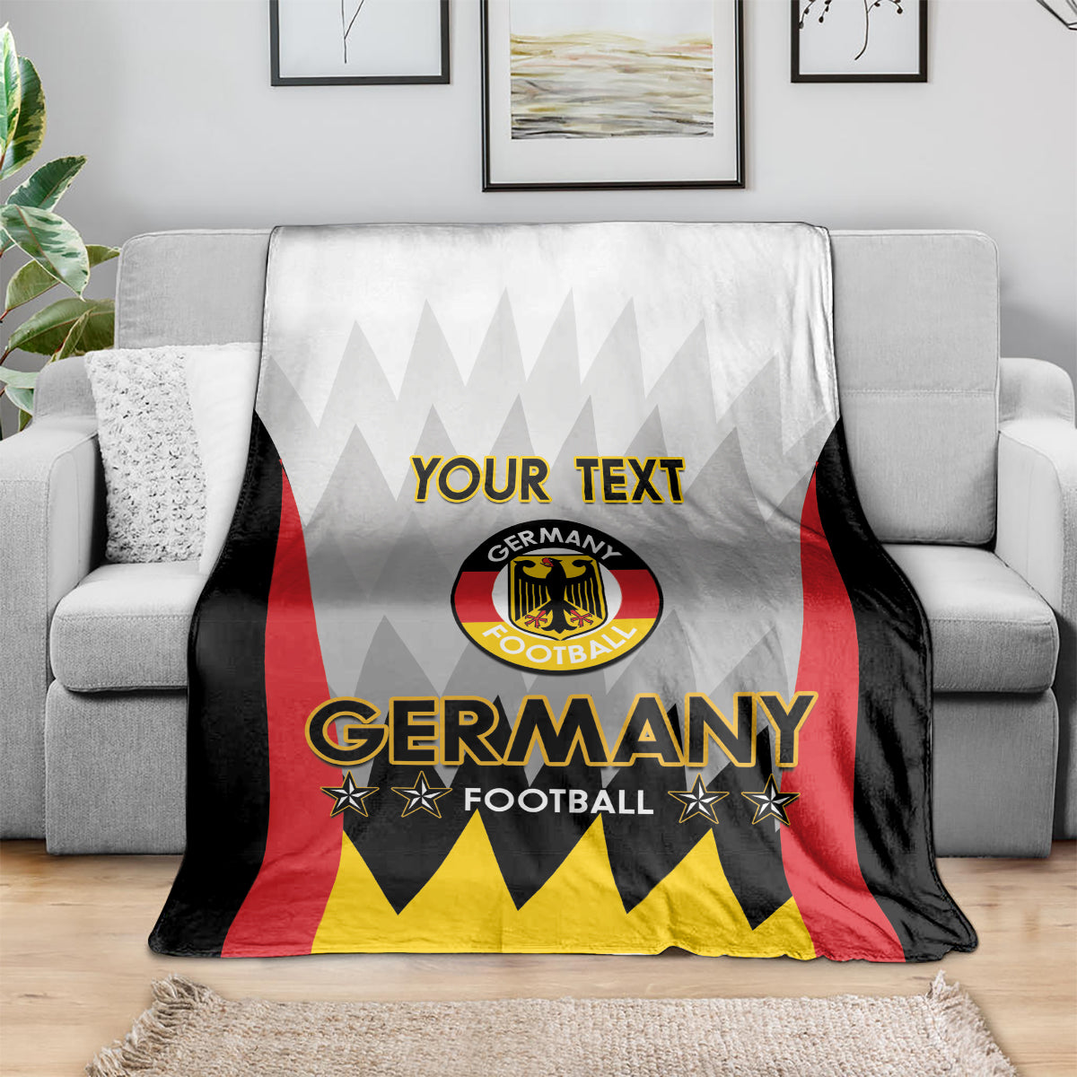 White Germany football blanket with “YOUR TEXT” and Germany crest on couch, red black yellow design