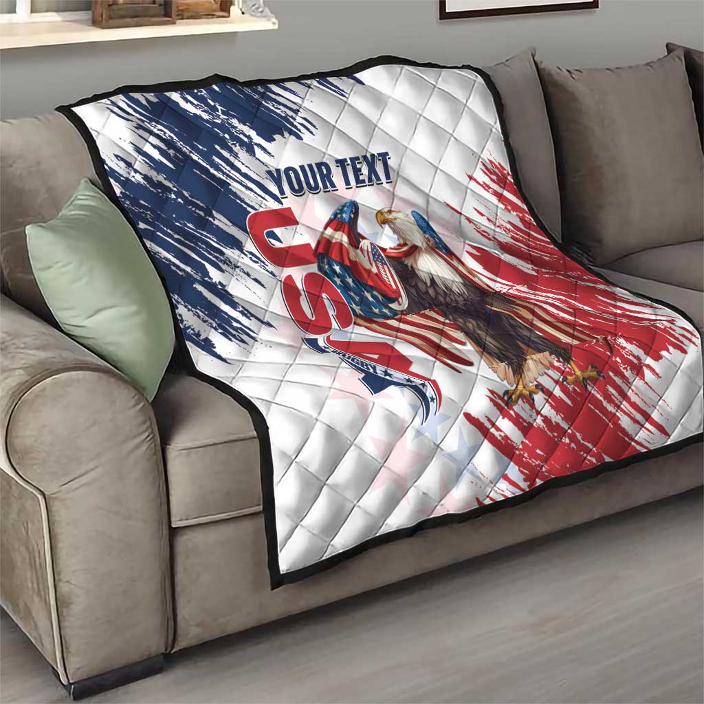 White quilt on gray sofa showing American flag eagle graphic across quilted surface.