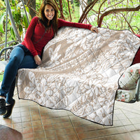 Beige quilt blanket with white tropical floral design and diamond quilting, black borders.