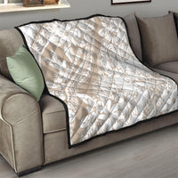Beige quilt throw with white floral and swirl pattern, diamond stitched surface, black trim.
