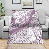 Purple and white floral Polynesian throw blanket spread on a gray sofa