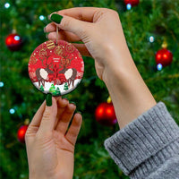 Red round ceramic Christmas ornament with caribou illustration and gold hanging loop, held in hand