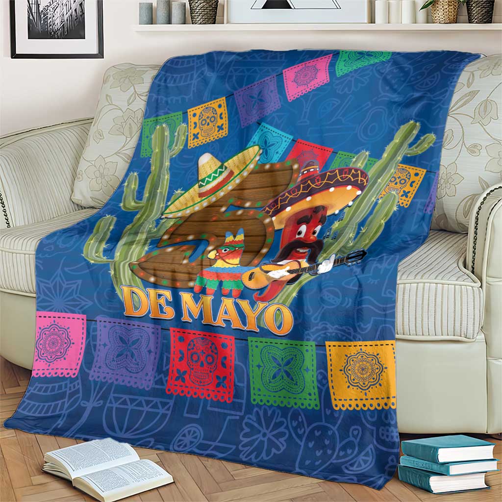 Blue blanket on sofa with 'DE MAYO' title, cactus, sombreros, and multicolor blocks