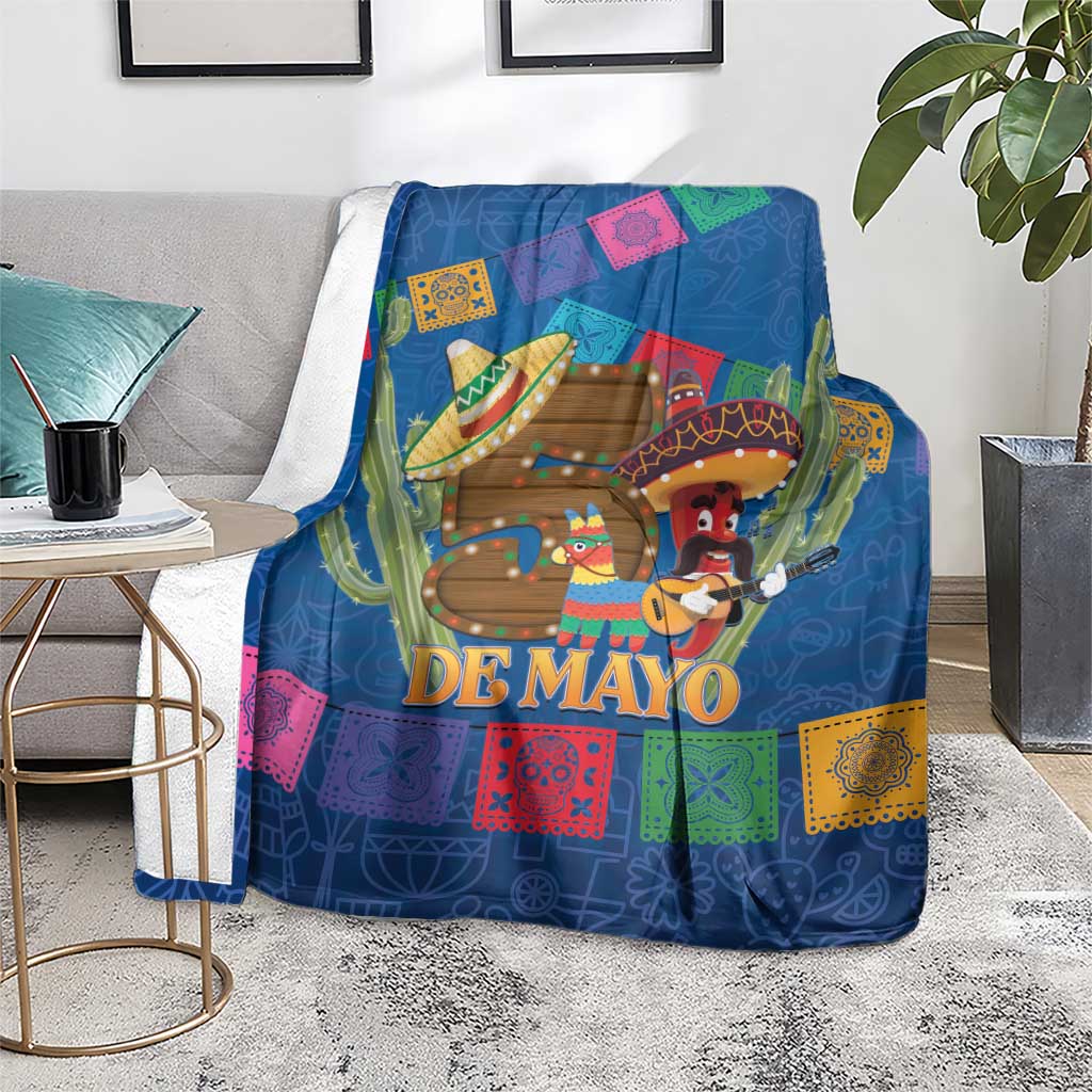 Blue blanket on gray chair with 'DE MAYO' design, cactus and sombrero characters