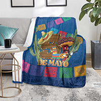 Blue blanket on gray chair with 'DE MAYO' design, cactus and sombrero characters