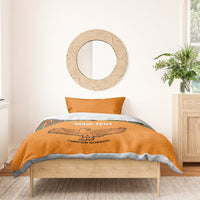Orange bedding set with two pillows and Kente border stripes, featuring a bird emblem