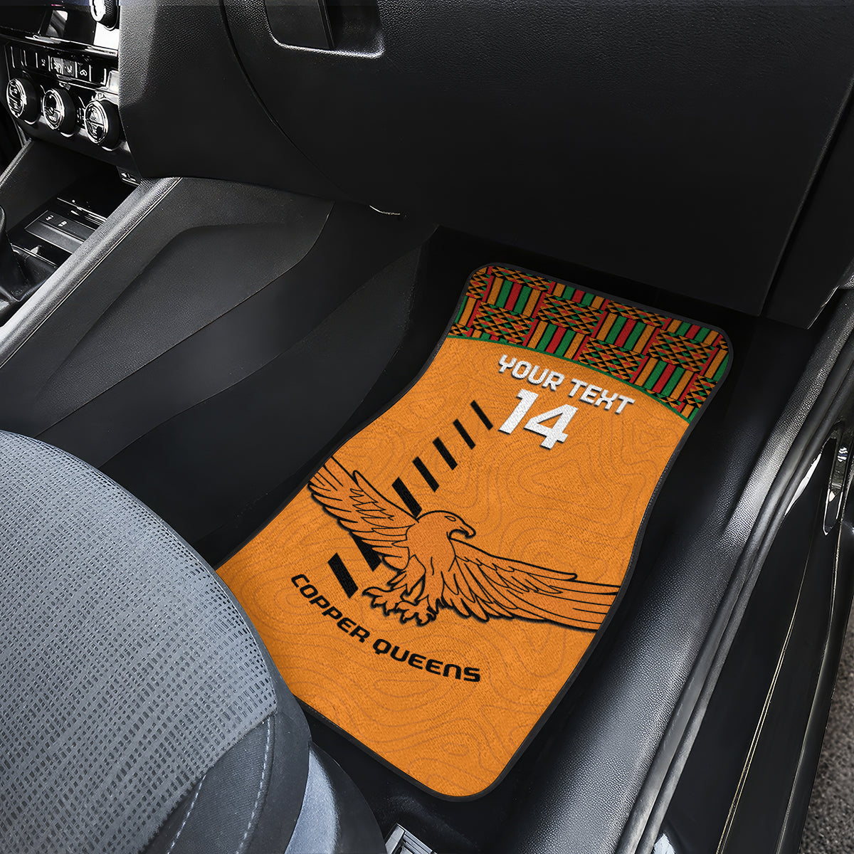 Orange car floor mat with Kente trim, eagle graphic, 'YOUR TEXT 14' and 'COPPER QUEENS' on seat.