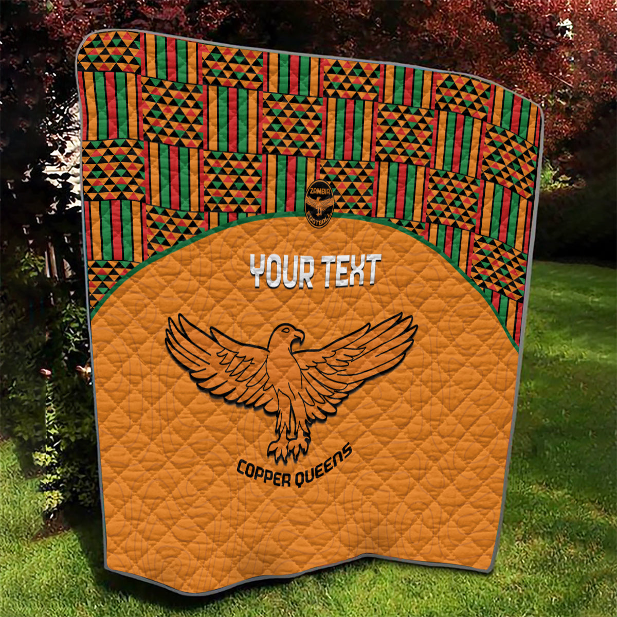 Orange quilt blanket with quilted texture, multicolor Kente border, and eagle emblem