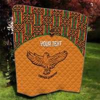 Orange quilt blanket with quilted texture, multicolor Kente border, and eagle emblem