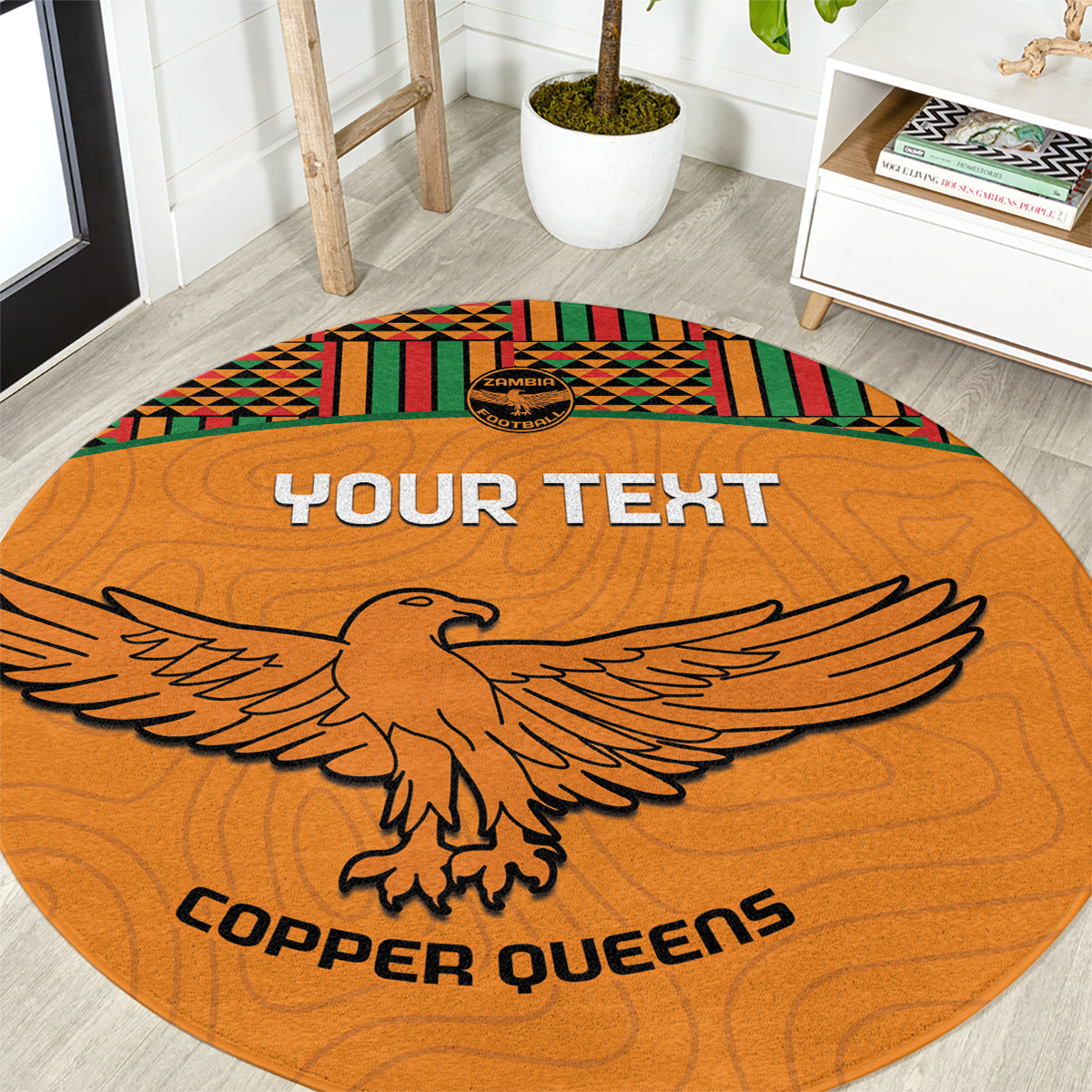 Orange round football rug with kente border, eagle graphic and 'COPPER QUEENS' text