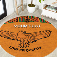Orange round football rug with kente border, eagle graphic and 'COPPER QUEENS' text