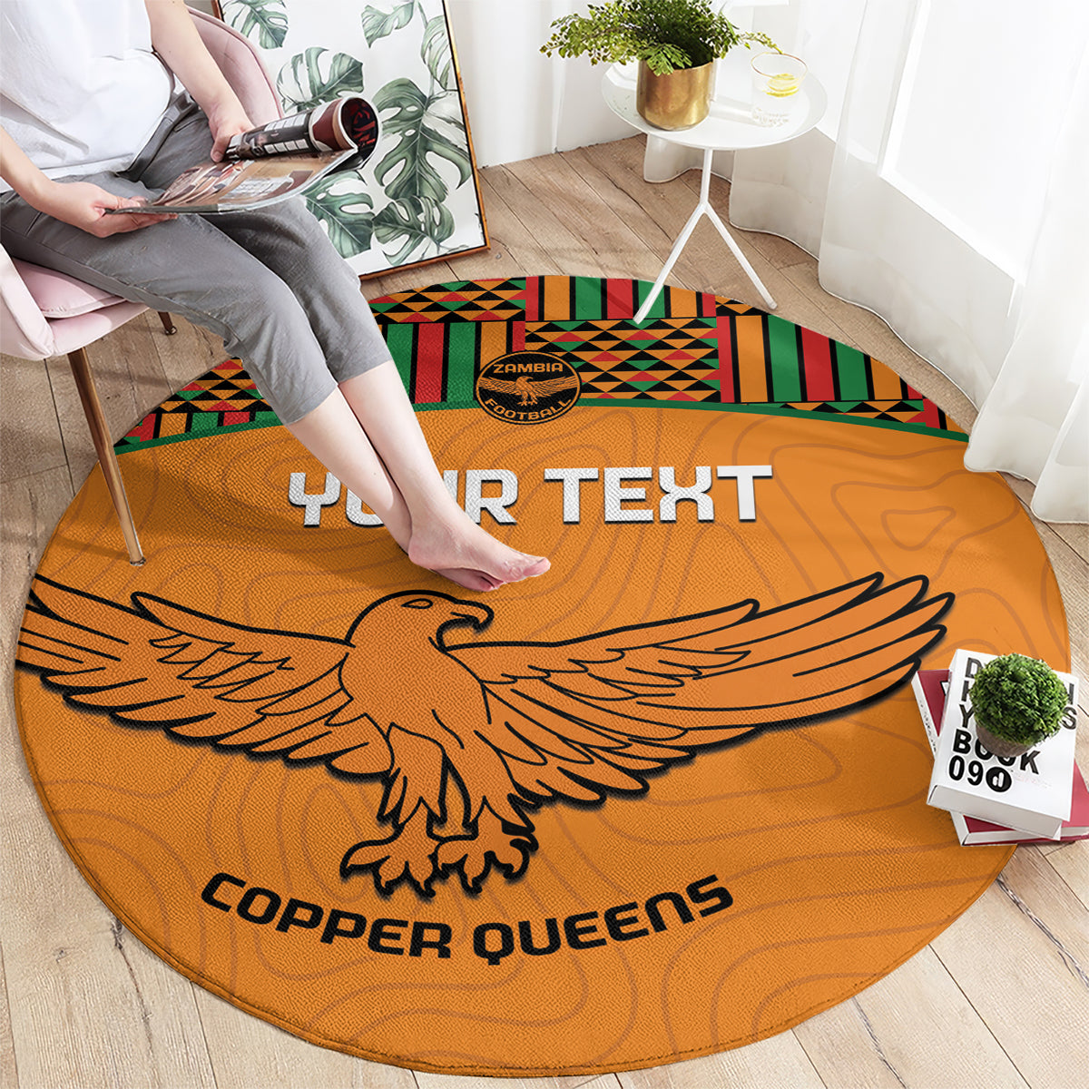 Orange round rug with 'YOUR TEXT,' eagle graphic, and multicolor kente striped edge