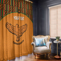 Orange window curtain with kente header, custom text, and winged bird emblem