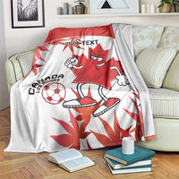 Canada soccer blanket draped on couch, red-and-white mascot with maple leaf and soccer ball
