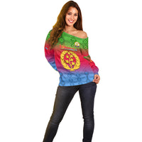 Off-shoulder gradient sweater with green, red, and blue kente pattern and gold crest on front