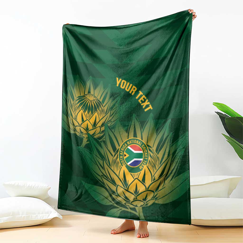 Green cricket blanket with gold crest and tropical leaves, held up to show full design