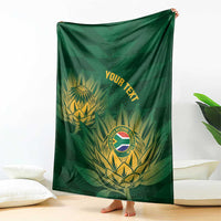Green cricket blanket with gold crest and tropical leaves, held up to show full design