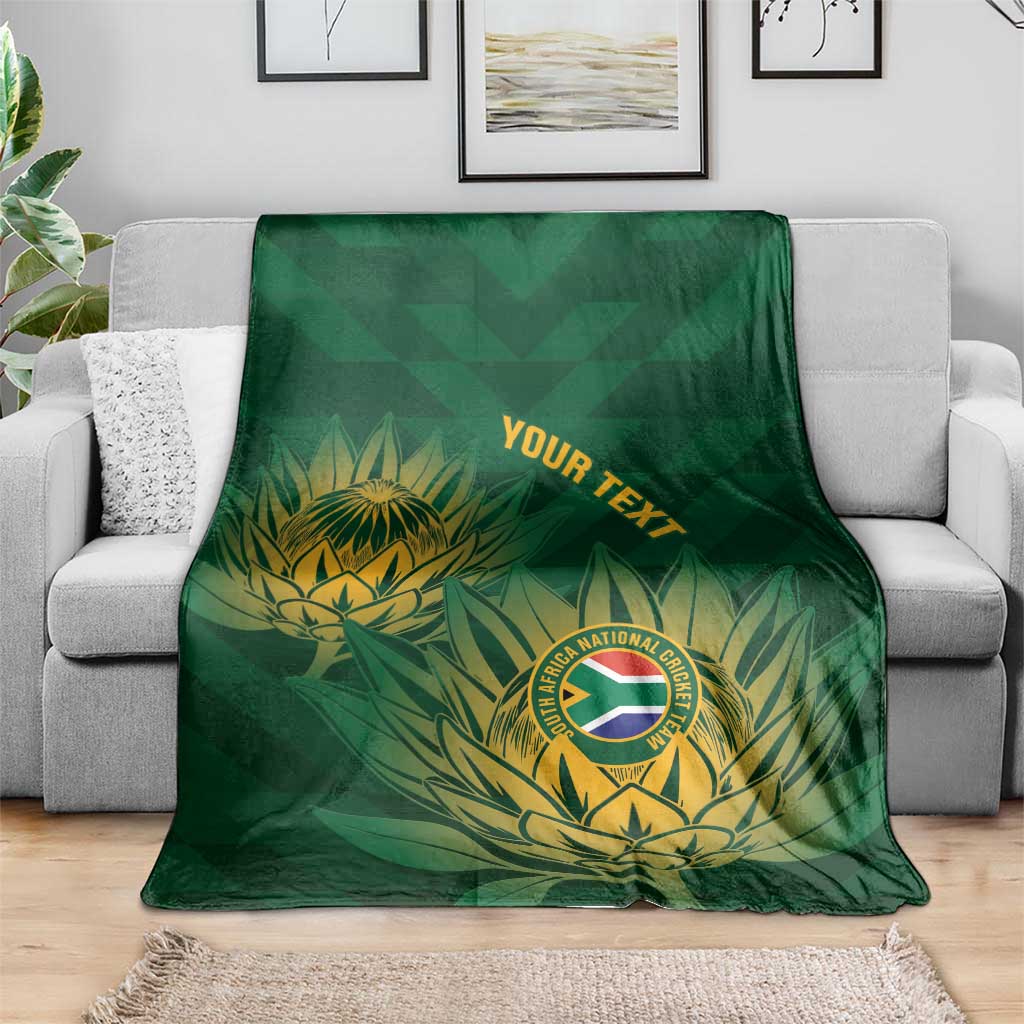 Green cricket blanket with gold crest and leaf pattern, folded and laid across a couch