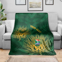 Green cricket blanket with gold crest and leaf pattern, folded and laid across a couch