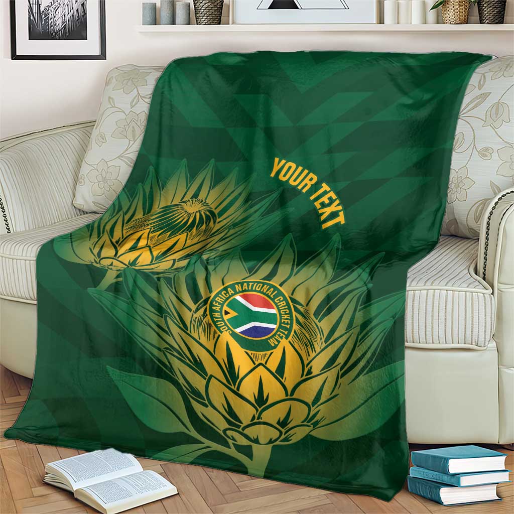 Green cricket blanket with gold crest and tropical leaves, covering a couch with books nearby