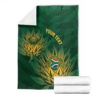 Green cricket blanket with gold crest and custom text, with rolled white towels beside it