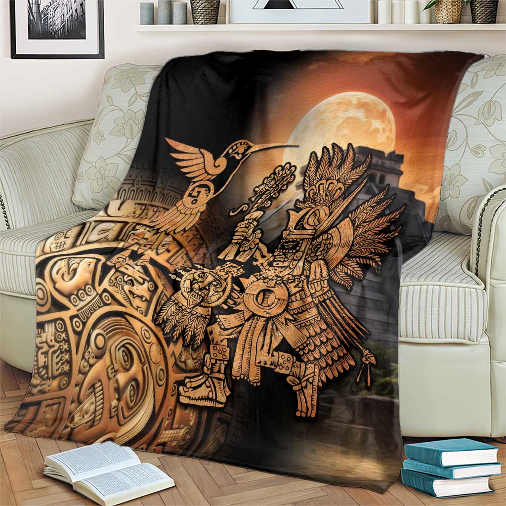 Black Aztec blanket with gold warrior and hummingbird, orange moon glow, on patterned couch