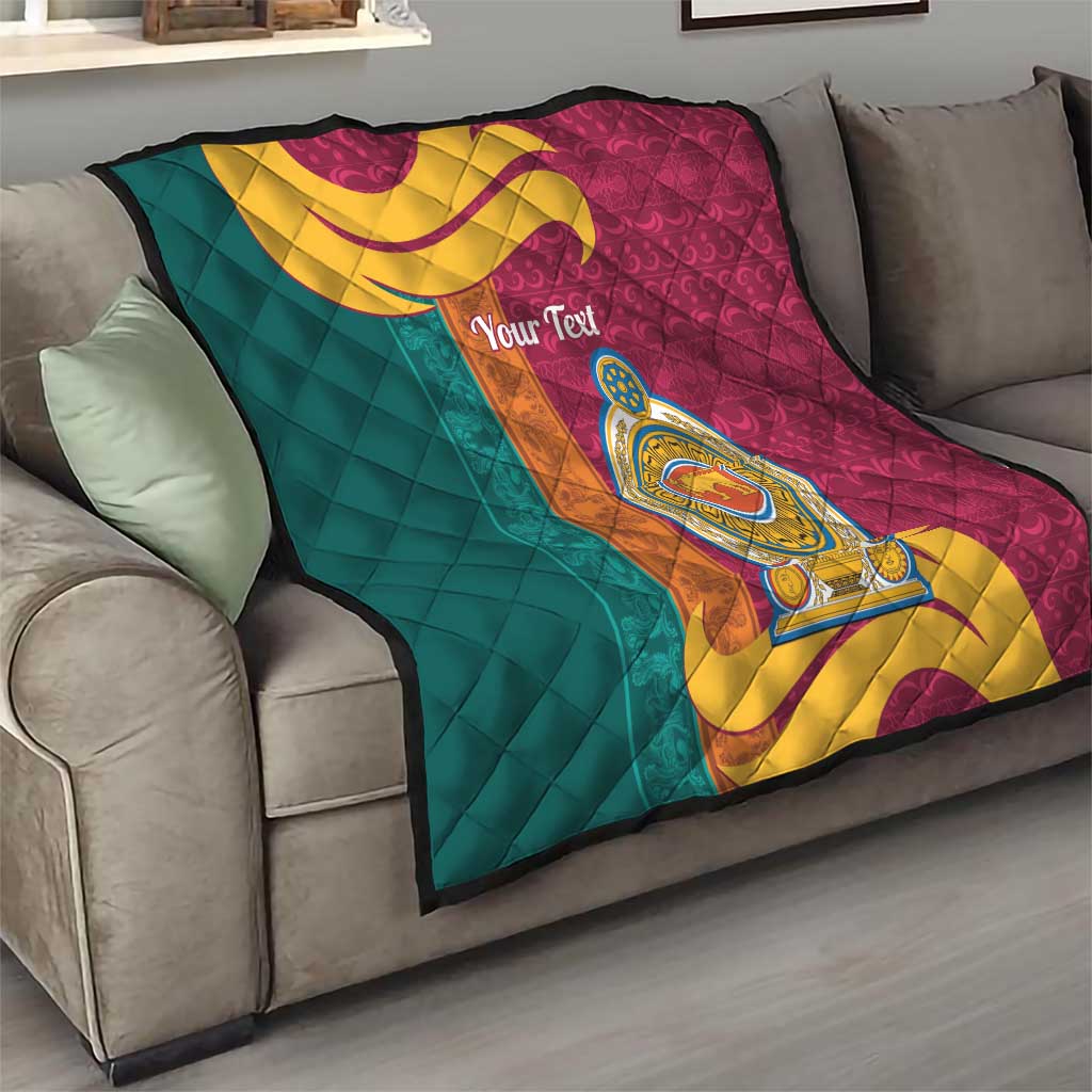 Teal and maroon quilt on gray sofa with gold crest medallion and swirling scroll, quilted.