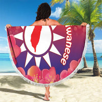 Round red beach blanket with white sun emblem and pink blossoms, fringed edge, held outdoors.