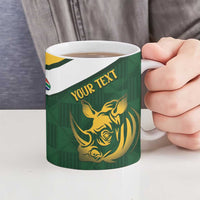 Green ceramic mug held by hand with gold rhino and “YOUR TEXT” graphic