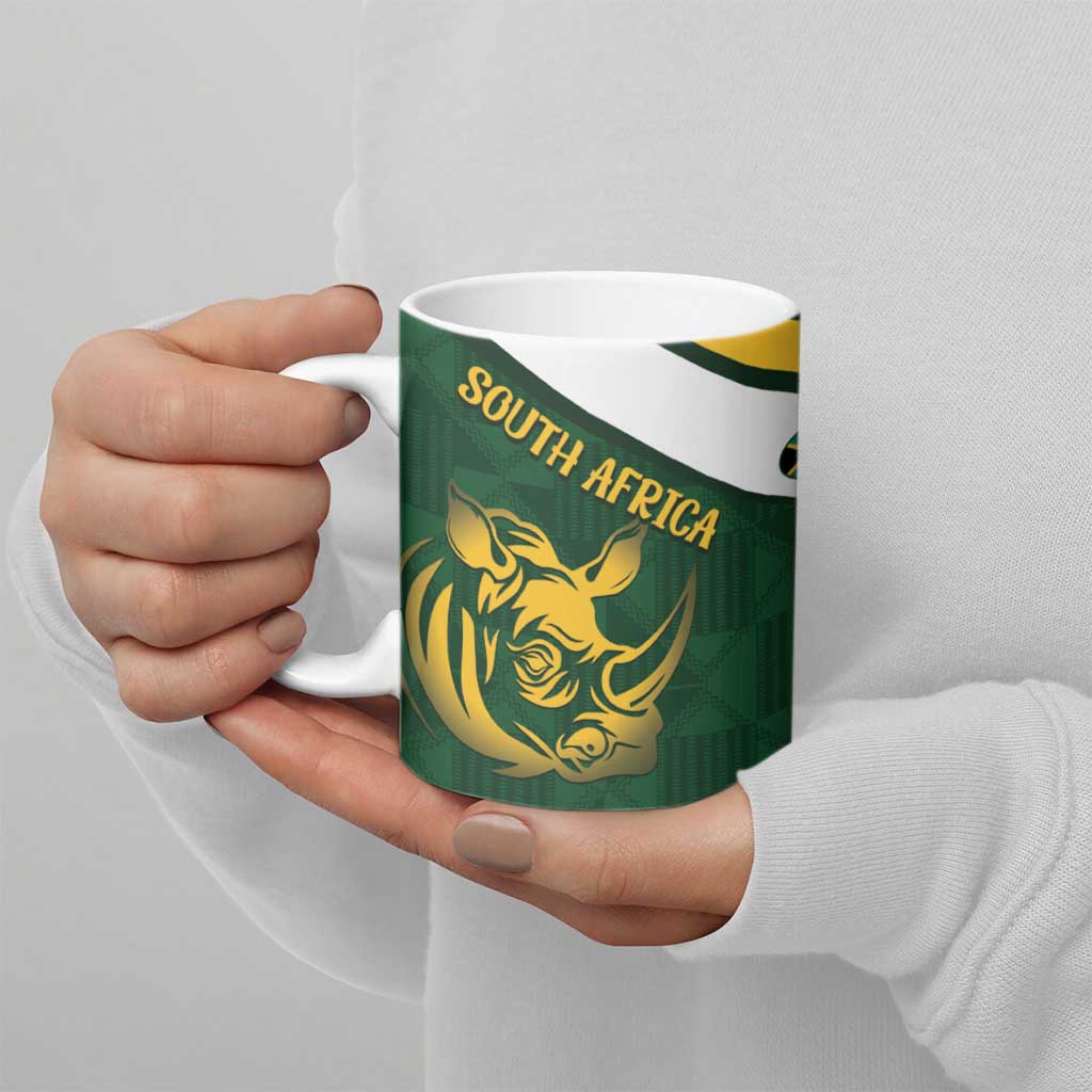 Green ceramic mug held by hand with gold rhino and “SOUTH AFRICA” label