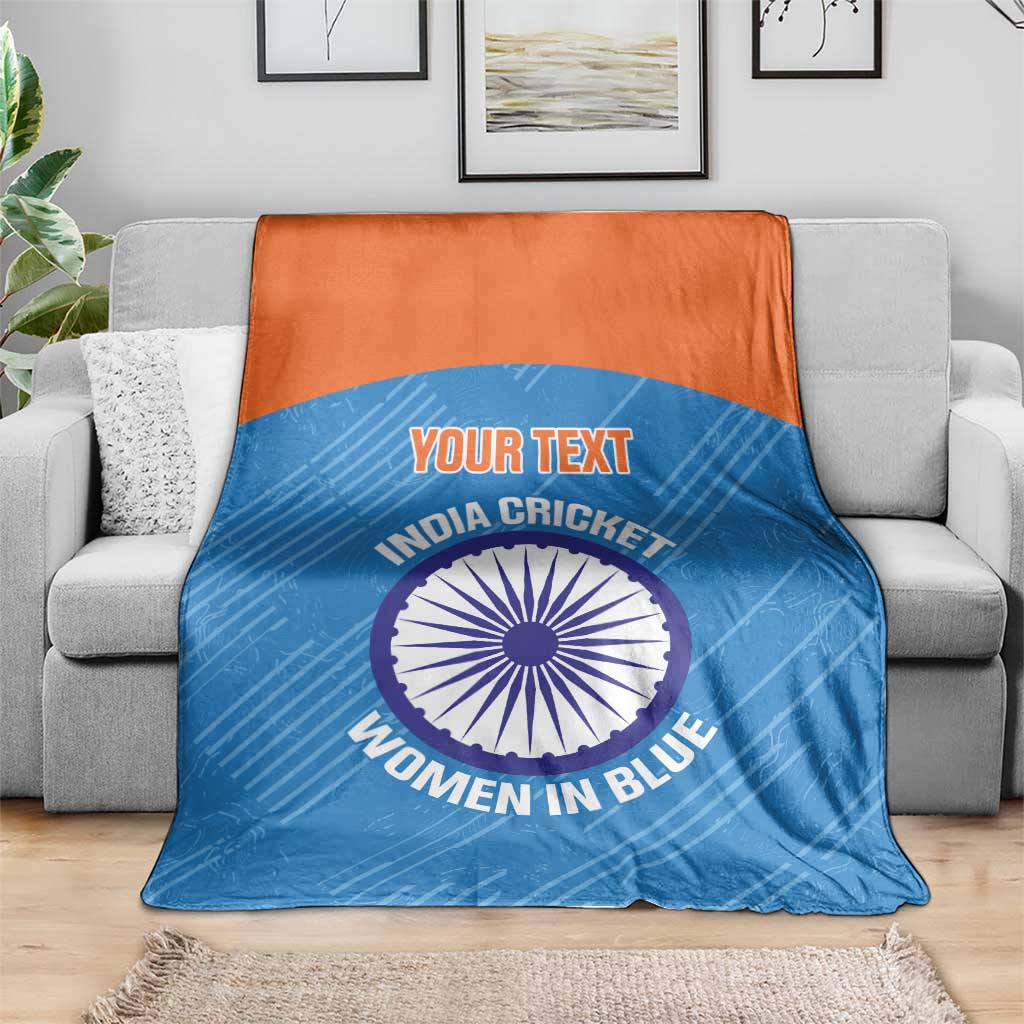 Blue cricket blanket with orange top band over gray sofa, circular India Women in Blue emblem