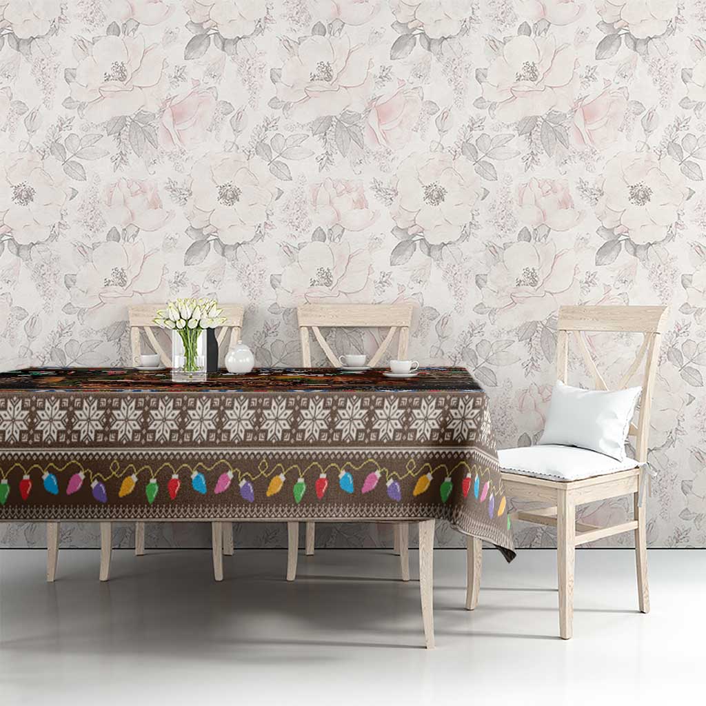 Christmas tablecloth on dining table, dark design with “Merry Yule” log artwork and colorful trim.