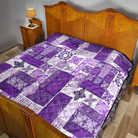 Purple and white quilt laid on a bed, patchwork squares with ornate floral motifs