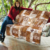 Brown patchwork quilt draped on a bench with white tiki and floral square designs