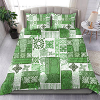 Green quilt bedding set spread with tropical leaf and geometric patchwork; two pillows shown