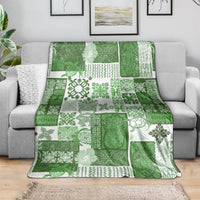 Green and white quilt blanket with tropical patchwork motifs, draped over a sofa.